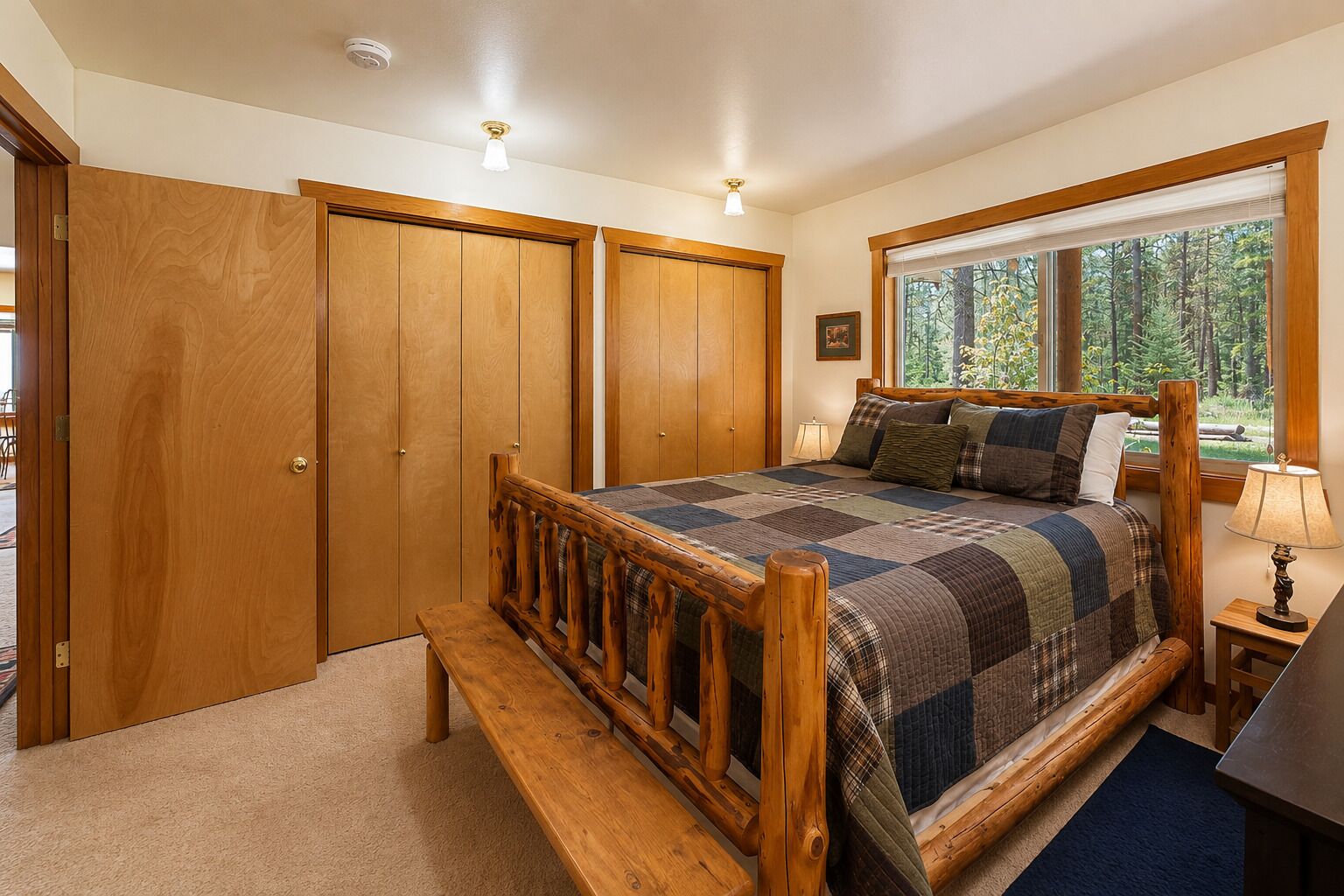 A bedroom with a wooden bed, a bench, a window with a view of trees, and a door.