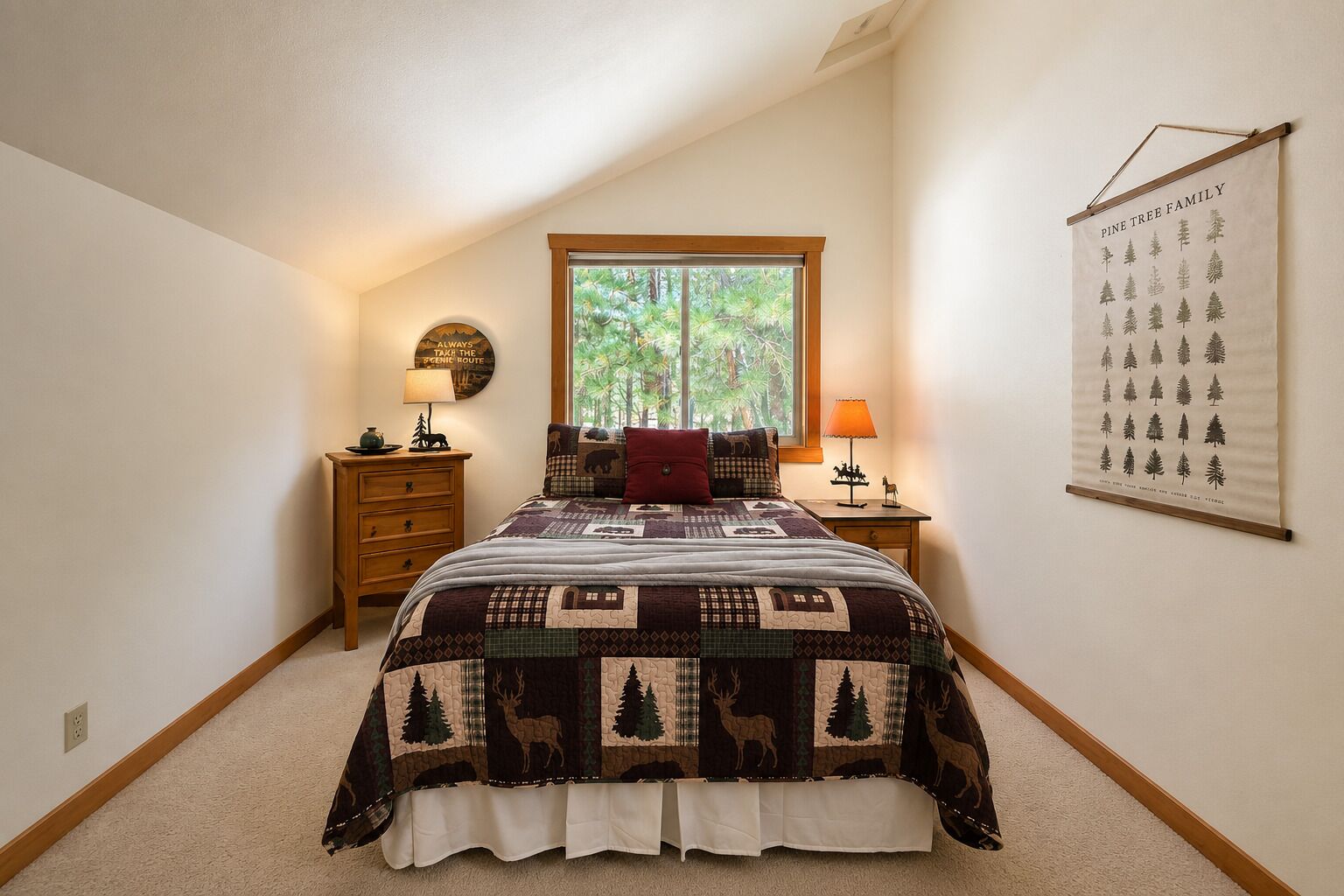 A bedroom with a large window, a quilt with forest and animal patterns, a wall-mounted poster, and two bedside tables with lamps.
