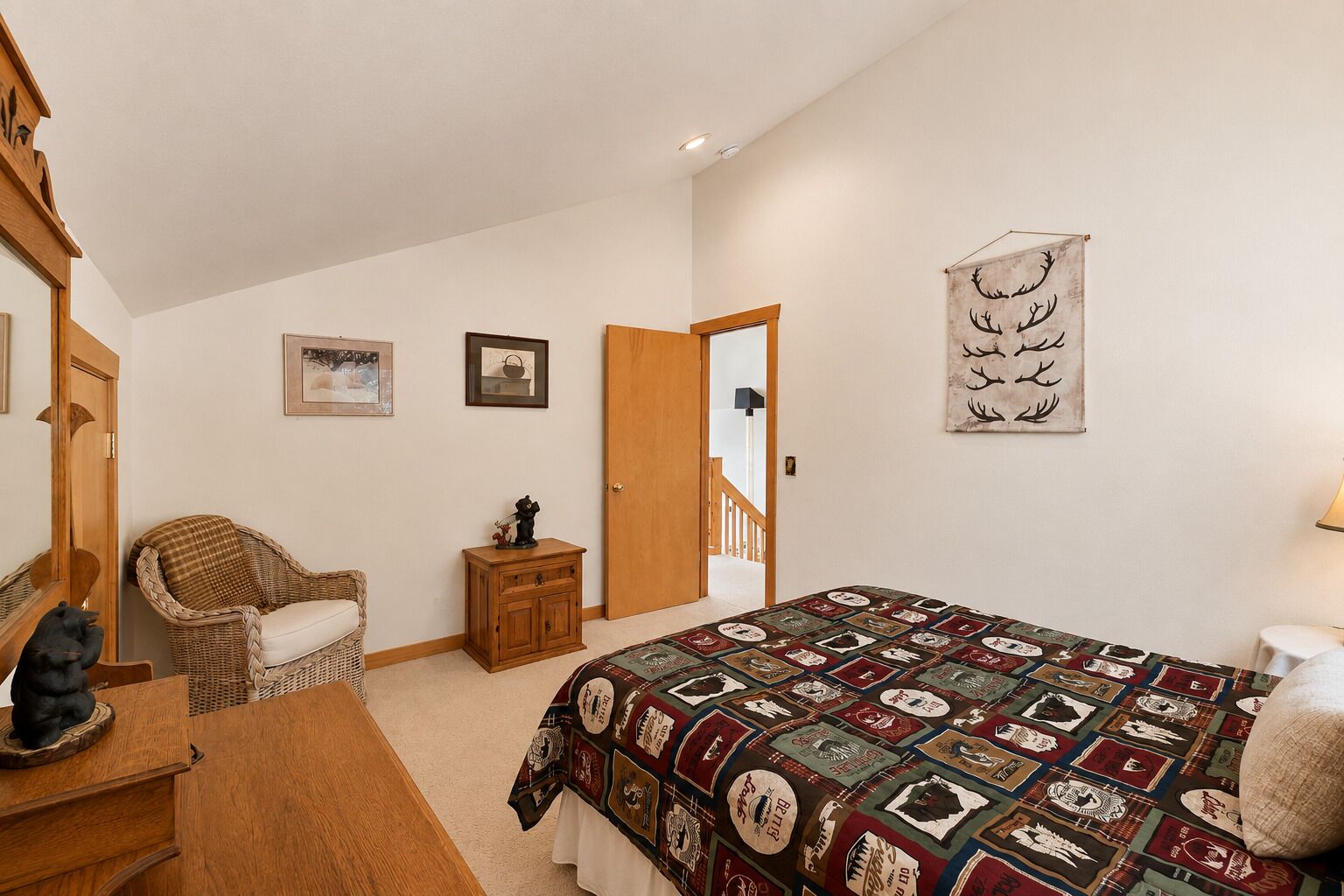 Un dormitorio con una cama grande, una silla, un armario pequeño, un espejo y una puerta que da a otra habitación.
