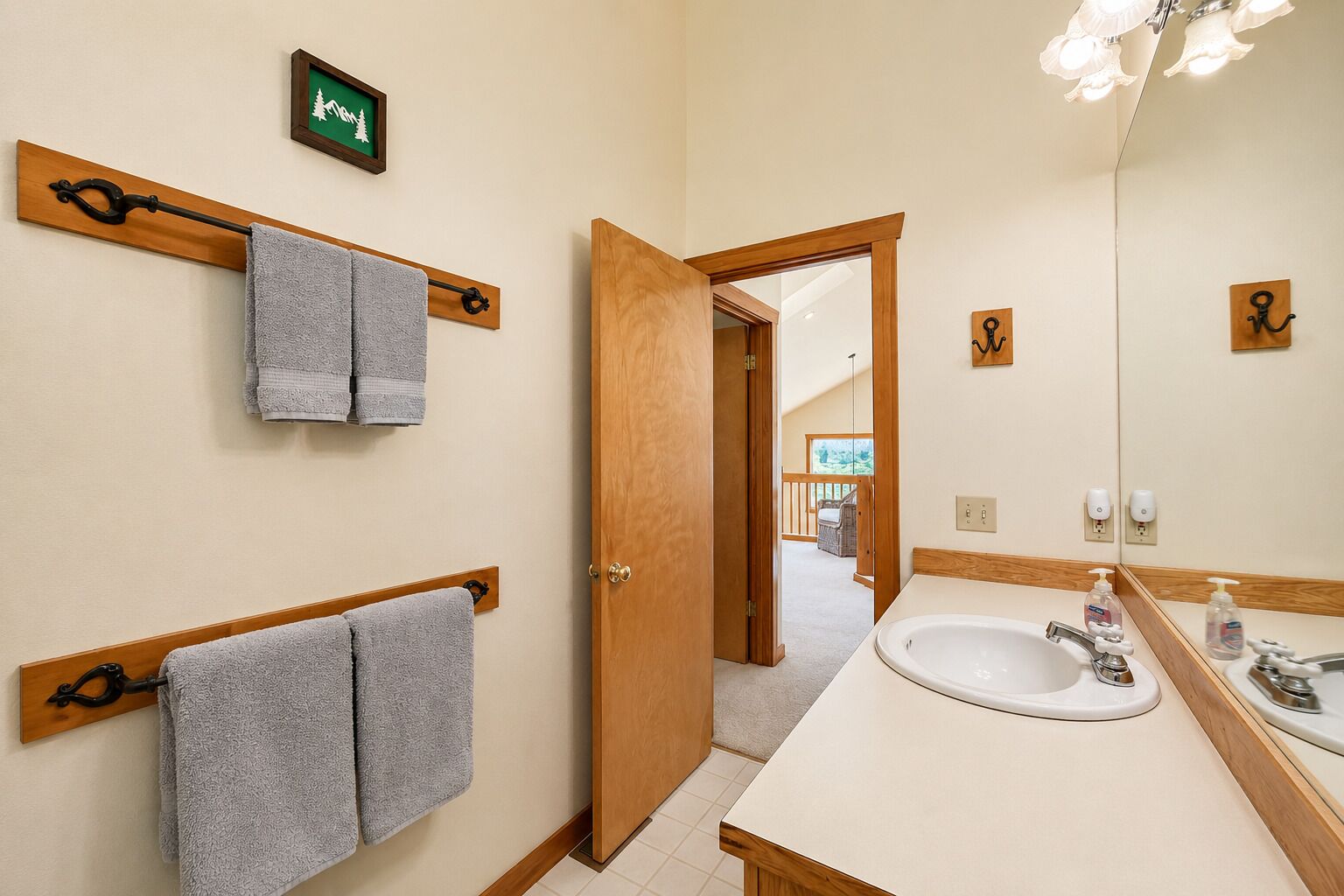 A bathroom with a wooden door, a sink with a mirror, and two towels hanging on hooks.