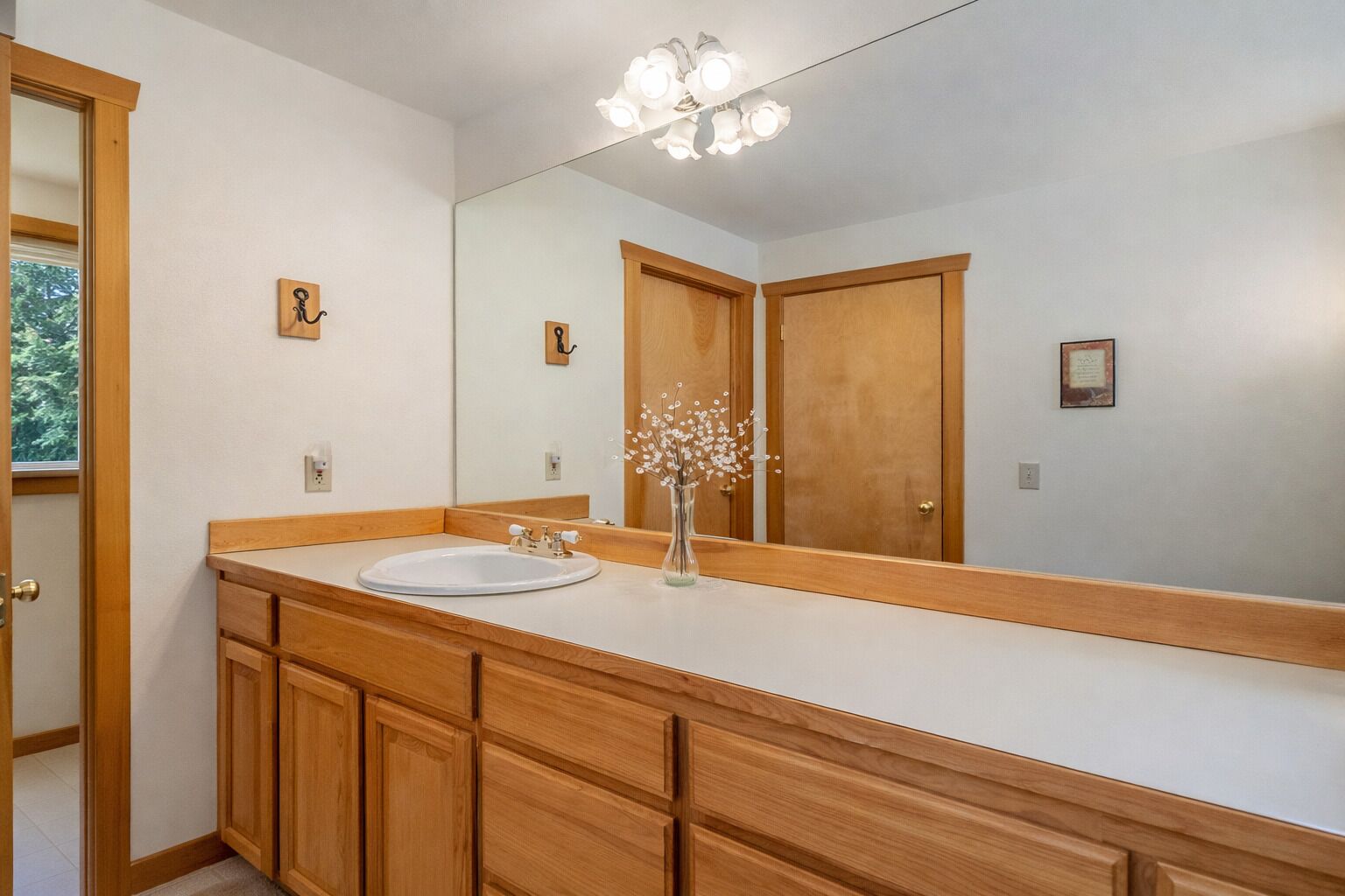 Une salle de bain avec un meuble-lavabo en bois, un grand miroir et un luminaire placé au-dessus du miroir.