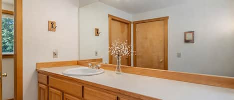 Une salle de bain avec un meuble-lavabo en bois, un grand miroir et un luminaire placé au-dessus du miroir.