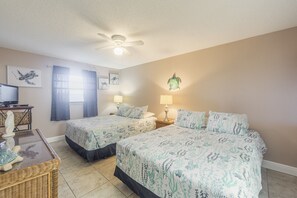 A bedroom with two beds, a ceiling fan, and a desk with a computer.