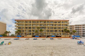 A multi-story hotel with balconies, a sandy beach in front, and umbrellas.