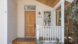 Une porte d’entrée en bois, avec le numéro « 448A » au-dessus, un porche blanc doté d’une balustrade et un petit arbre au premier plan.