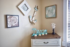 Um quarto com penteadeira, parede adornada com obras emolduradas e um objeto decorativo com conchas.