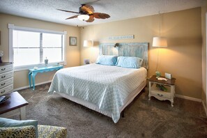 A bedroom with a bed, a nightstand, a dresser, a window, and a ceiling fan.