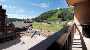 A view from a balcony overlooking a ski resort with buildings, a ski lift, and a mountainous backdrop.