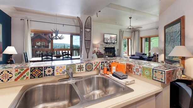 A kitchen with a large sink, colorful backsplash tiles, and a dining area with a view of a mountain.