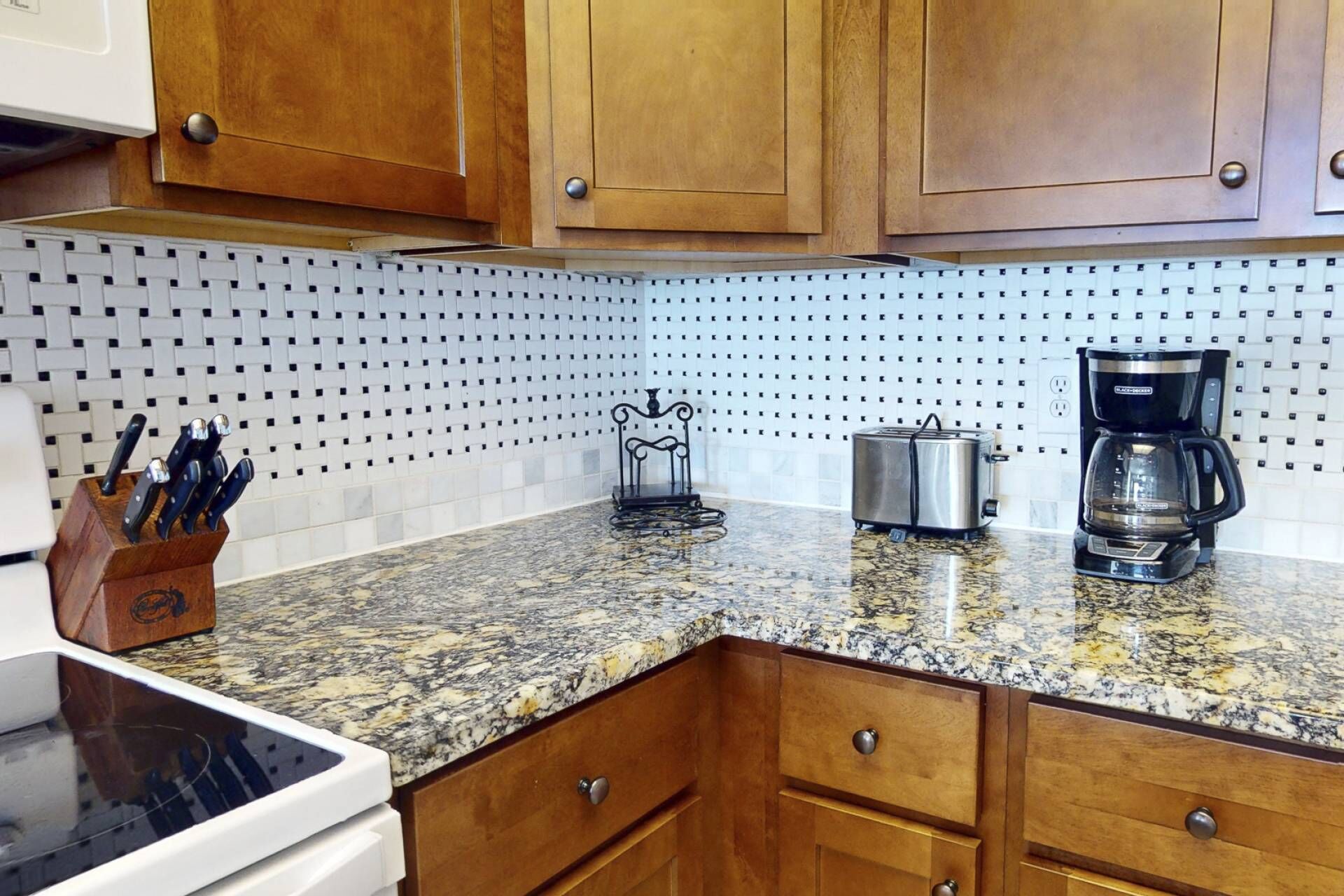 A kitchen with wooden cabinets, a granite countertop, a coffee maker, a toaster, and a knife block.