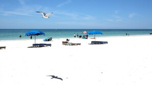 Une plage de sable blanc, avec des parasols bleus et des chaises longues.