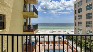 Vue depuis un balcon donnant sur une plage, avec une piscine et des chaises longues.