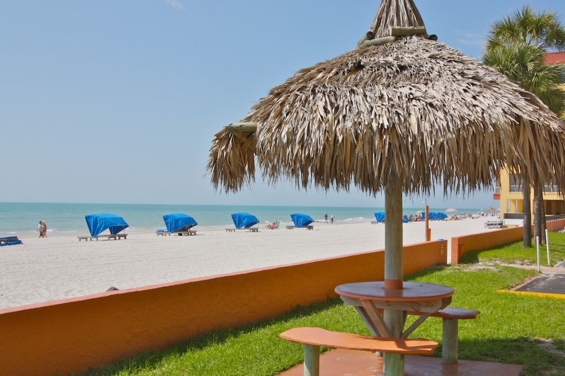 A beach with thatched umbrellas, lounge chairs, and a picnic table.