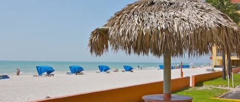 A beach with thatched umbrellas, lounge chairs, and a picnic table.