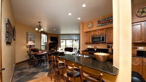 A kitchen with a large island, wooden bar stools, a microwave, and a coffee maker. - Professionally Decorated Peregrine Point Steps to Lifts (Durango)