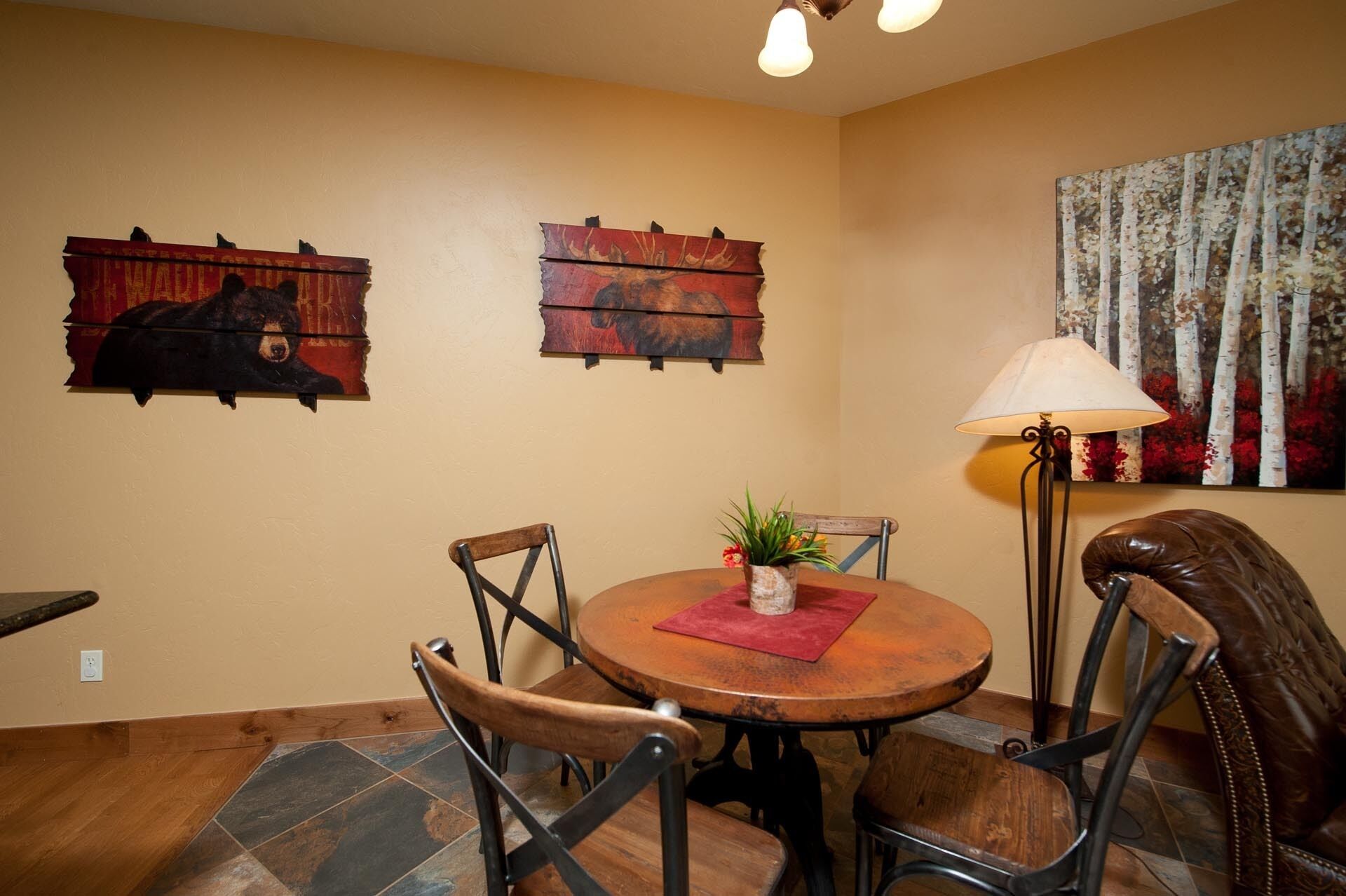 Un coin repas comprenant une table ronde en bois, quatre chaises, un vase avec des fleurs et deux œuvres d’art en bois fixées au mur.