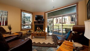 A living room with a fireplace, a television, and a large window overlooking a balcony. - Professionally Decorated Peregrine Point Steps to Lifts (Durango)