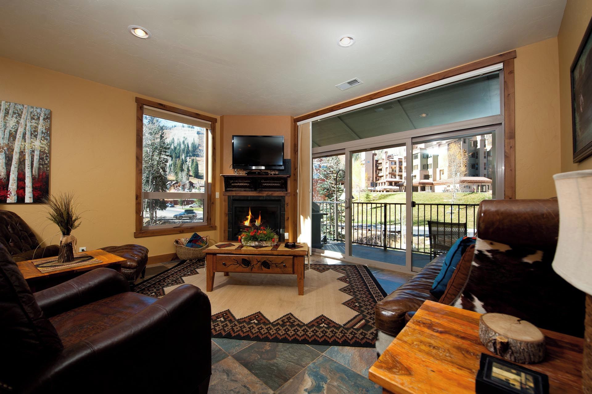 A living room with a fireplace, a television, and a large window overlooking a balcony.