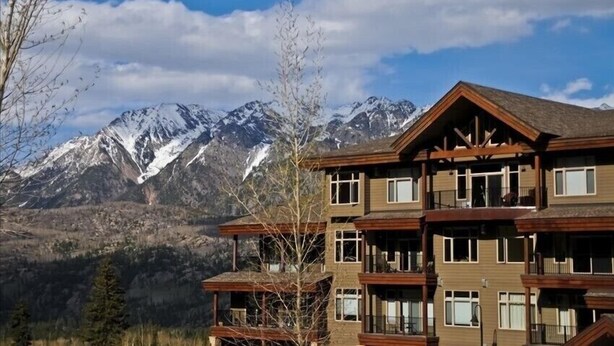 A multi-story building with balconies, set against a backdrop of snow-capped mountains and clear skies. - Professionally Decorated Peregrine Point Steps to Lifts (Durango)