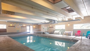 Une piscine intérieure aux murs carrelés, au sol en béton et au plafond orné de poutres apparentes et de luminaires.