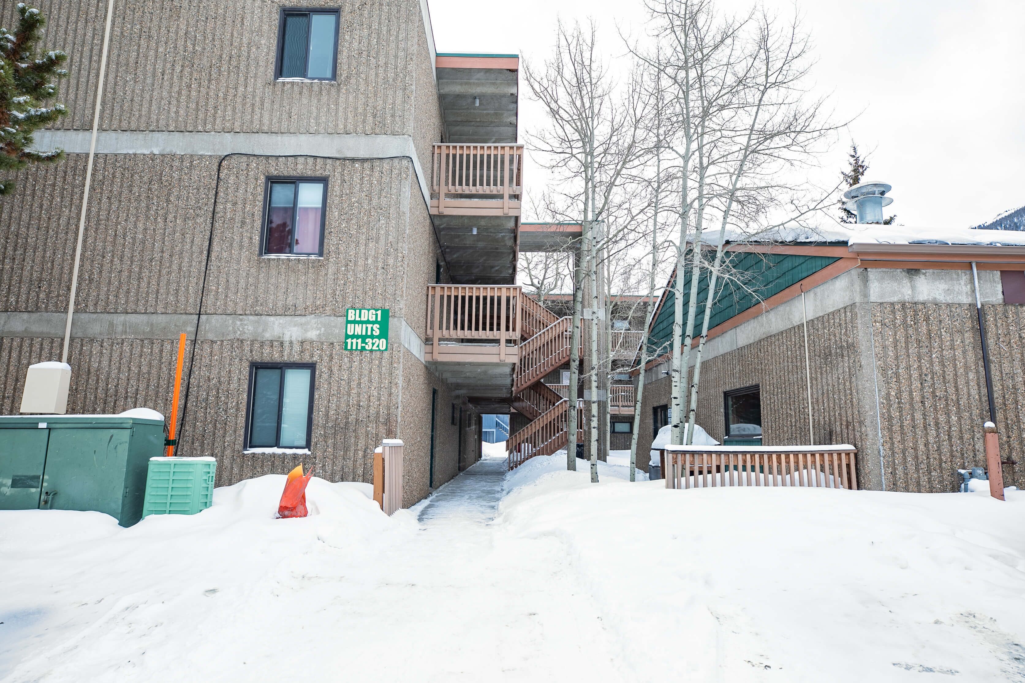 A multi-story building with balconies, a sign indicating 'Bldg1 Units 111-320', and a snow-covered ground.