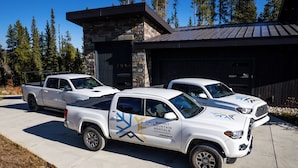 Trois camionnettes blanches sont garées devant un bâtiment à la façade en pierre et au toit métallique.