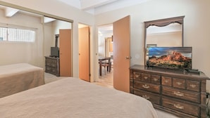 Une chambre avec deux lits, une commode, un téléviseur et un miroir.