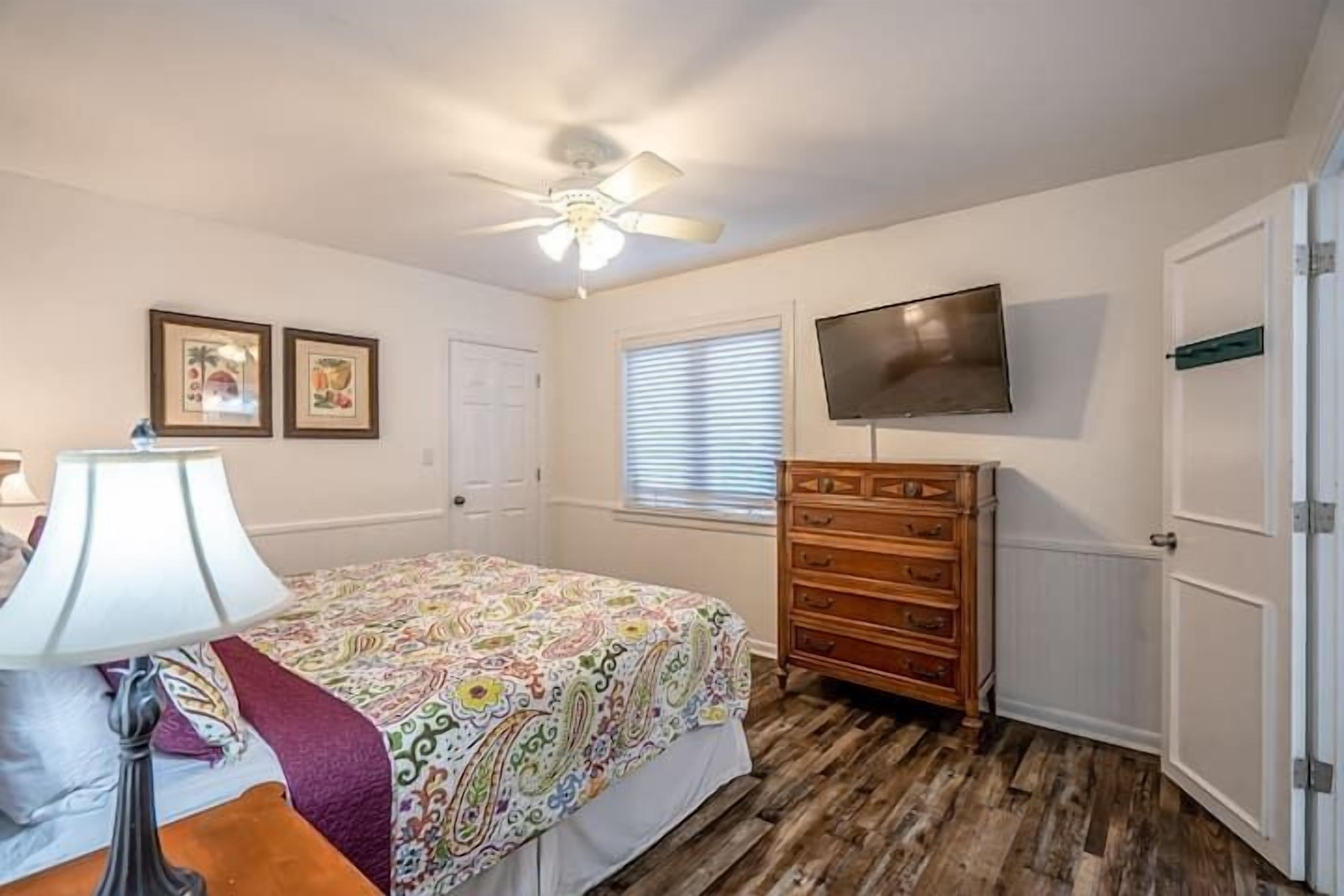 Un dormitorio con cama, cómoda, televisor y ventilador de techo.