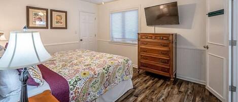 Un dormitorio con cama, cómoda, televisor y ventilador de techo.