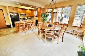 A spacious kitchen with wooden cabinets, a dining area with a large table and chairs, and a view of the outdoors through large windows. - Pool, Hot Tubs. 4 Suites! Walk to Main Street Dining, Shops. Near Rec Path (Frisco)