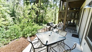 Een terras buiten met een tafel, stoelen, een barbecue en uitzicht op een bebost gebied.