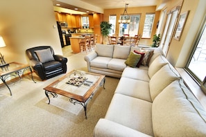 A living room with a sofa, armchair, and coffee table. There is a kitchen in the background with wooden cabinets and a dining area with a table and chairs. - Pool, Hot Tubs. 4 Suites! Walk to Main Street Dining, Shops. Near Rec Path (Frisco)