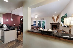 A modern kitchen with a central island, a dining area with a brown leather couch, and a fireplace with decorative items.