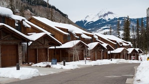 Une rangée de cabanes en bois aux toits enneigés, se dressant sur un fond de montagnes et d’arbres.
