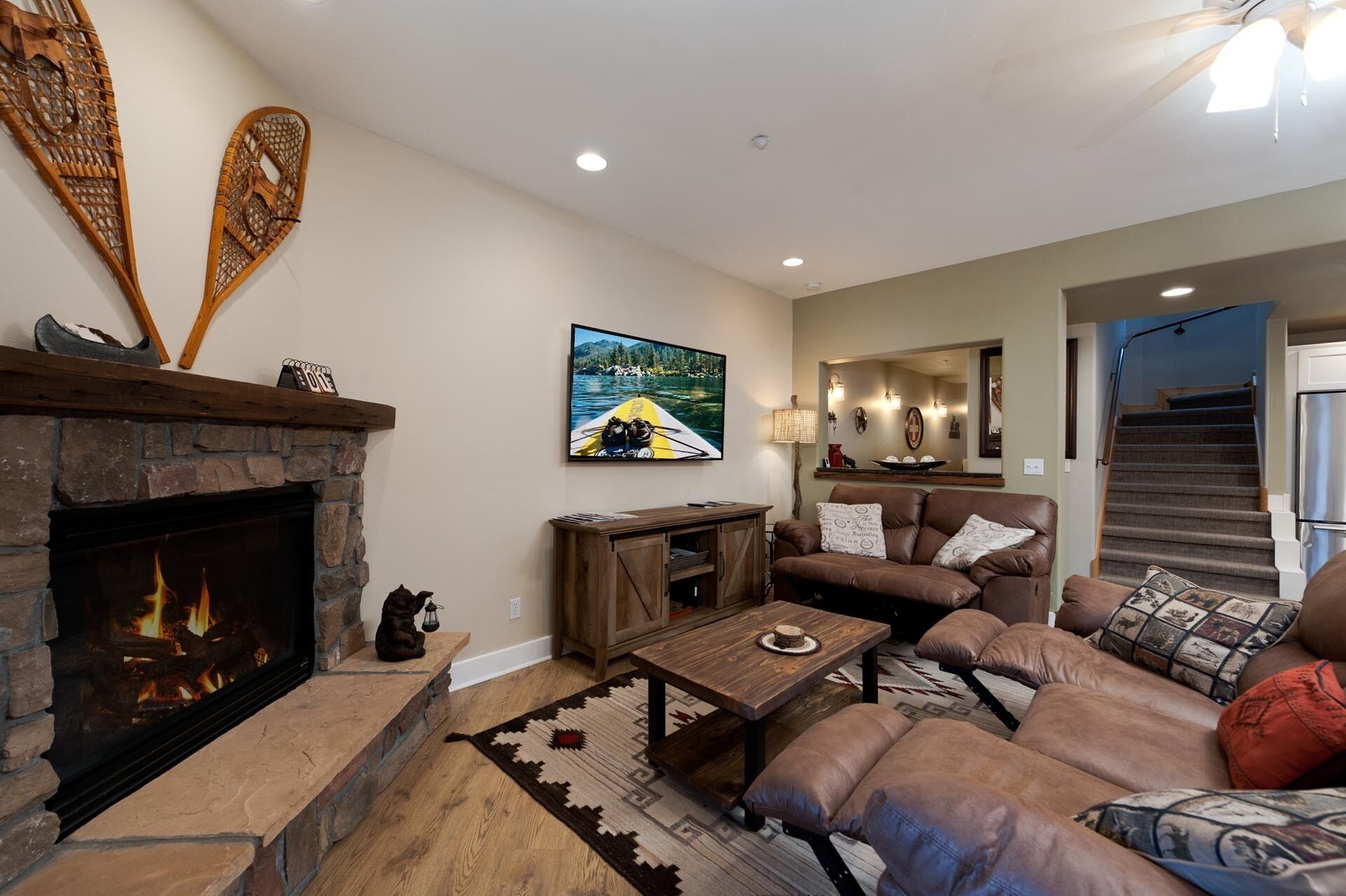 A cozy living room with a fireplace, a large couch, a coffee table, and a painting of a canoe on water.