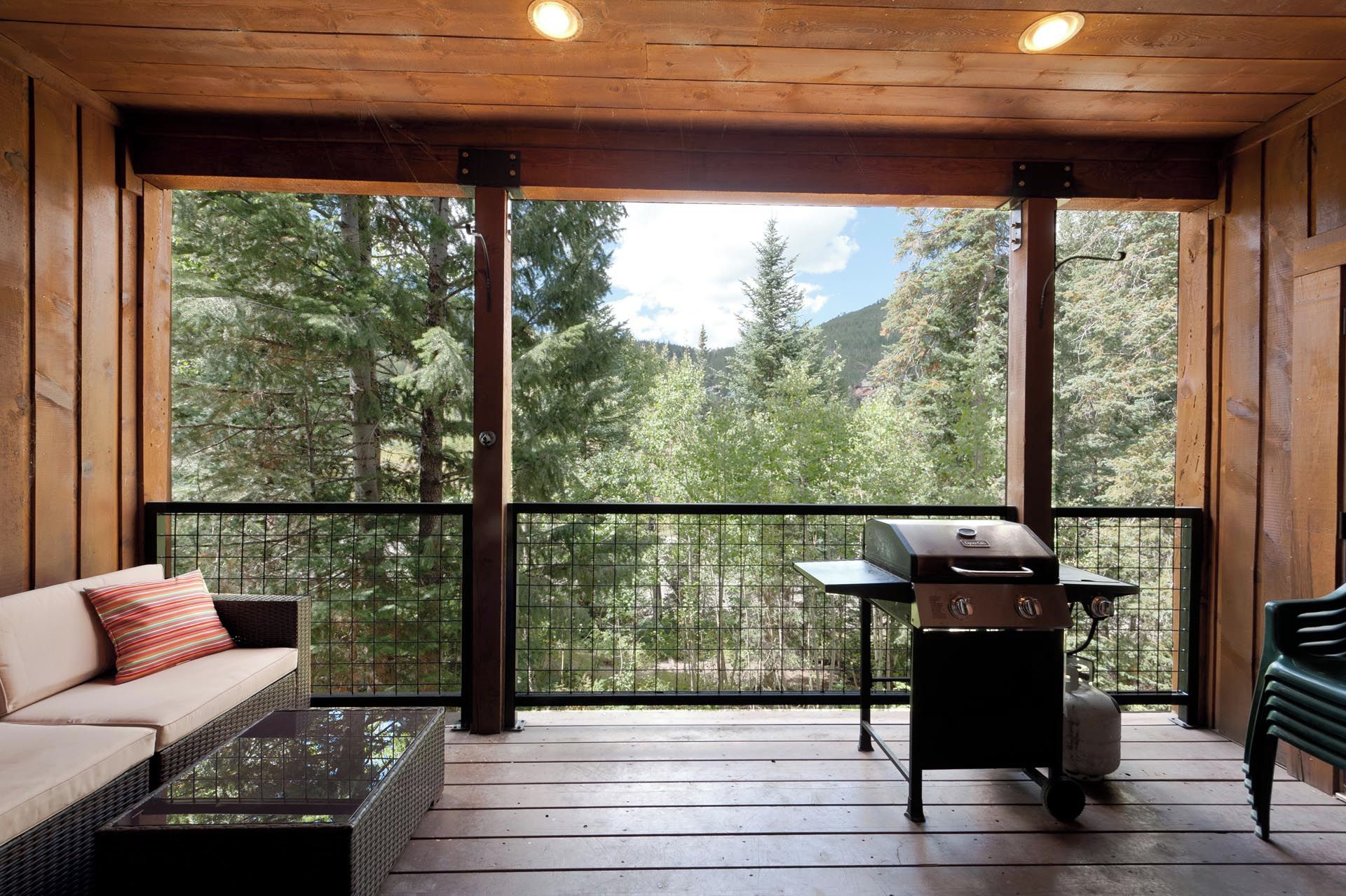 A covered balcony with a grill, a sofa, and a view of a forested mountain area.