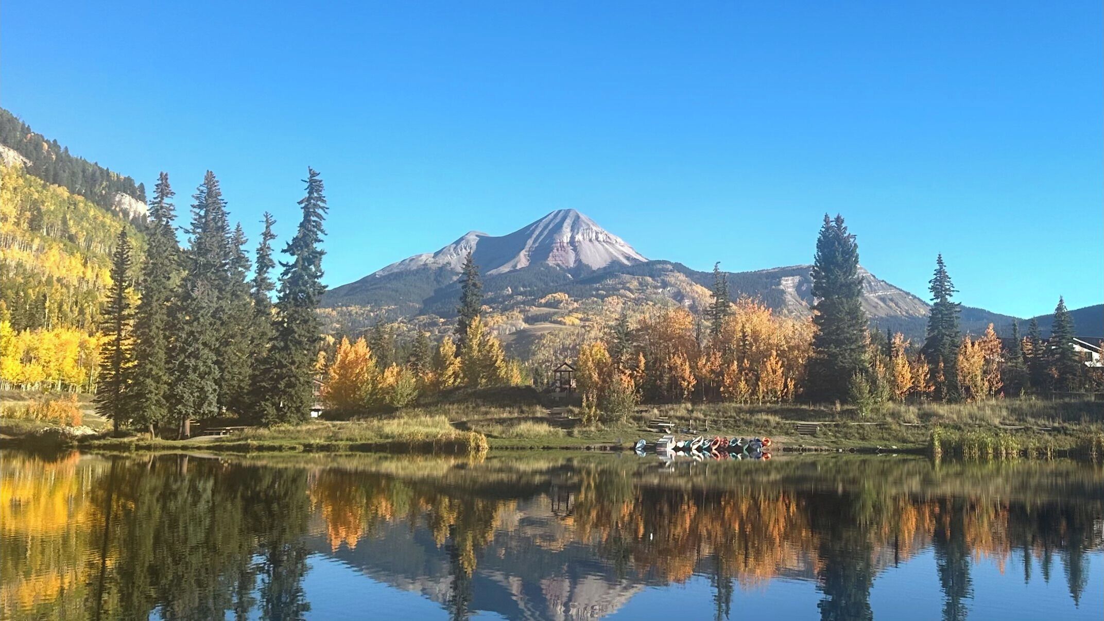 A mountain landscape with a lake reflecting trees and a gazebo.