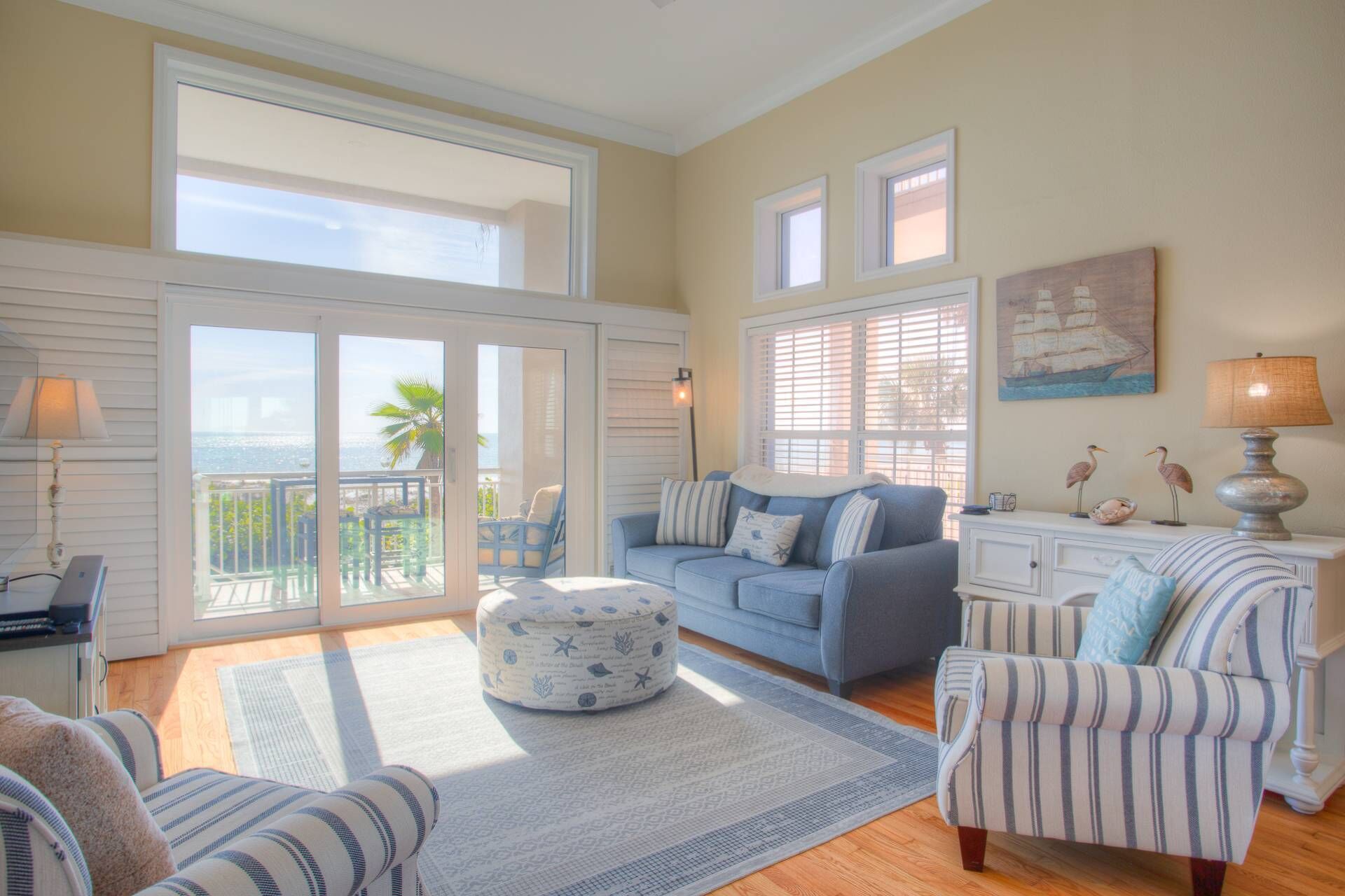 A spacious living room with a large sliding glass door leading to a balcony, a blue sofa, striped armchairs, and a small ottoman.