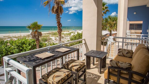 A balcony with a view of the beach, a table with a grill, and a sofa with patterned cushions.