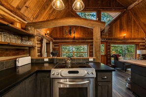 A rustic cabin interior with a kitchen featuring a stove, oven, and a dining area with a table and chairs.