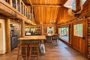 Interior de una cabaña de troncos con cocina, comedor y un cartel que dice 'CABINS'.