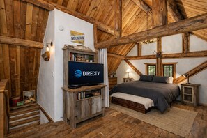 Une chambre rustique avec un plafond en bois, un lit, un téléviseur fixé au mur et un panneau indiquant l’heure « heure des montagnes ».
