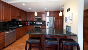 A modern kitchen with wooden cabinets, a stainless steel refrigerator, a granite countertop, and three bar stools. - Sitzmark townhome at Purgatory - Awesome views - Steps to slopes (Durango)