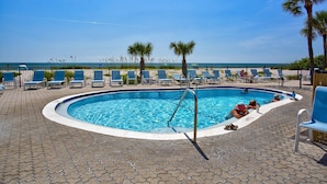 A swimming pool with lounge chairs and palm trees, overlooking a beach.