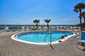 A swimming pool with lounge chairs and palm trees, overlooking a beach.