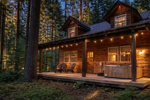 Eine Holzhütte mit Veranda, zwei Fenstern und einer Deckterrasse mit Stühlen und Grill.