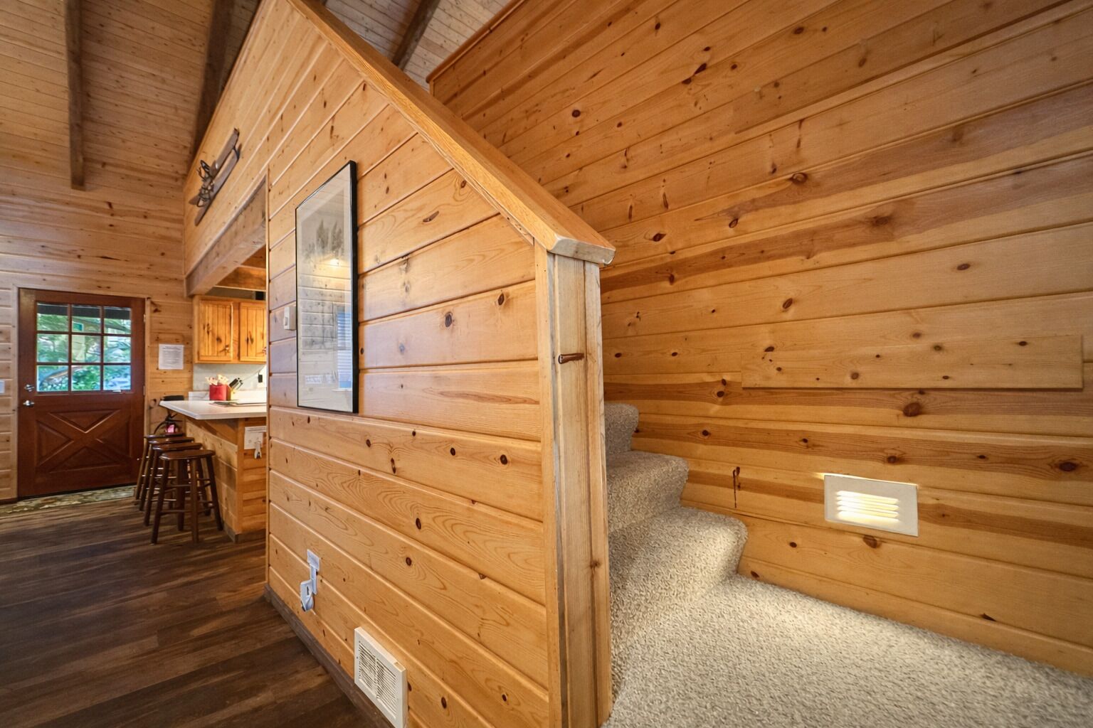 Een houten chalet van binnen, met een keukenhoek, een trap en een deur naar buiten.