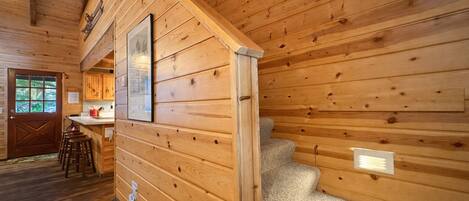 Een houten chalet van binnen, met een keukenhoek, een trap en een deur naar buiten.