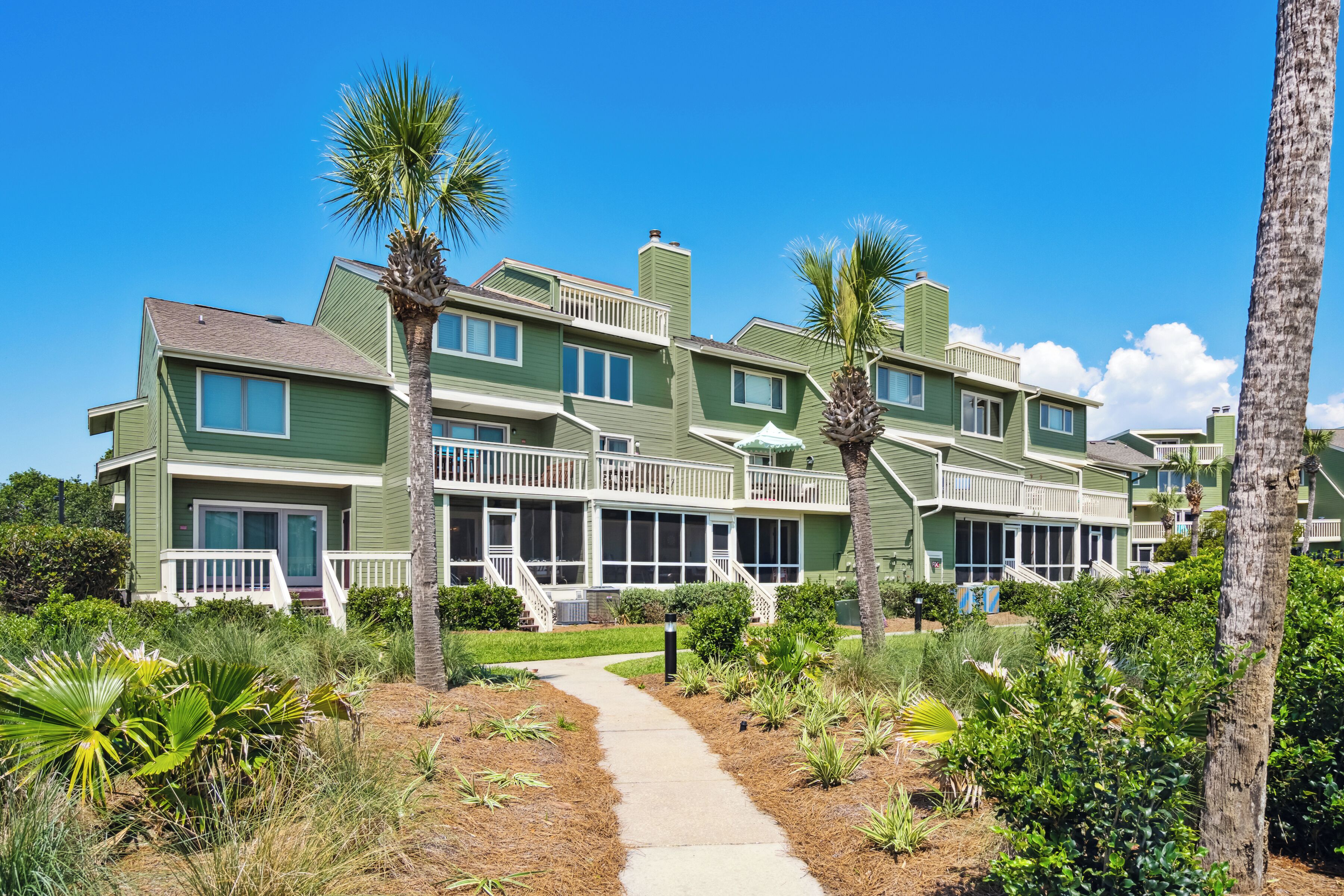 A multi-story hotel with a green exterior, multiple balconies, and a pathway leading to the entrance.