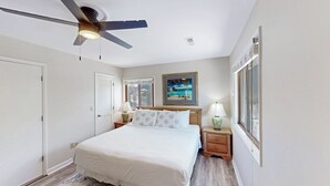 Una camera da letto con un letto, un ventilatore a soffitto, un comodino con una lampada, una finestra e un quadro appeso al muro.
